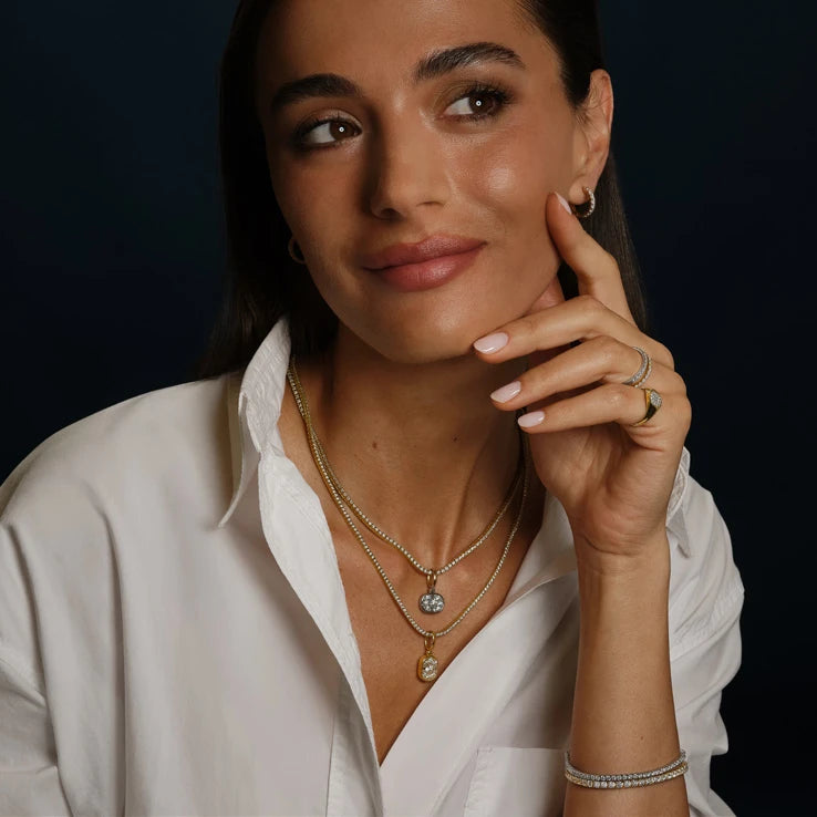 Woman in a white shirt wearing a diamond ring, layered gold necklaces and a tennis bracelet
