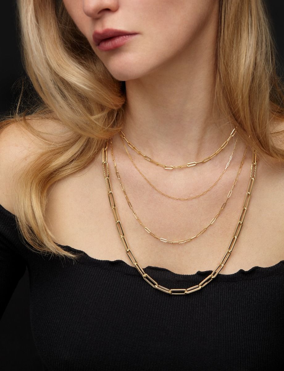 Model wearing layered yellow gold chains over a black top