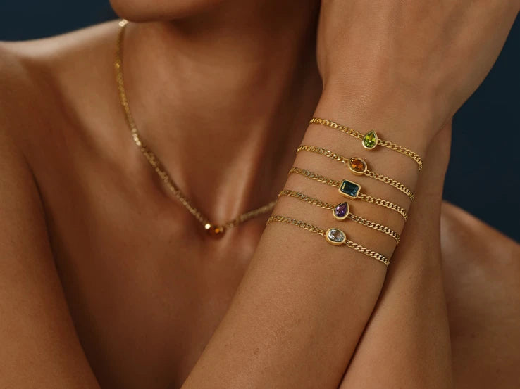 Stack of gold chain bracelets with colored stones on a woman's wrist
