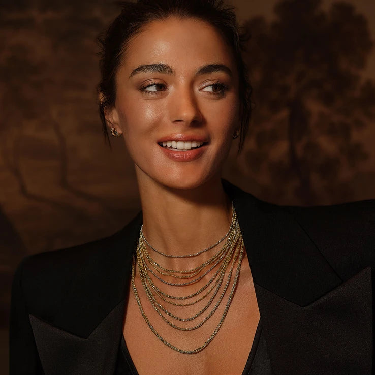 Woman in a black blazer wearing layered gold chain necklaces and gold bracelets